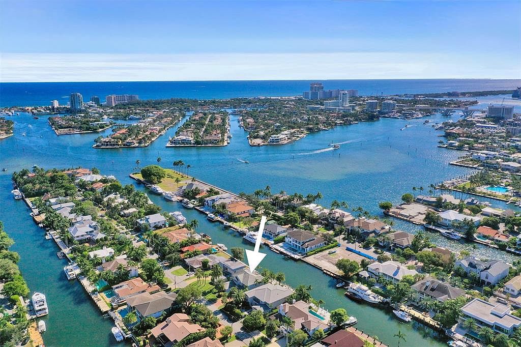 This aerial shot showcases a luxurious waterfront property nestled among a network of canals and waterways. The house features a gray roof, lush landscaping, and a private dock, emphasizing its prime location and access to boating. The surrounding neighborhood is characterized by similar high-end homes, creating an impression of an exclusive and desirable community.