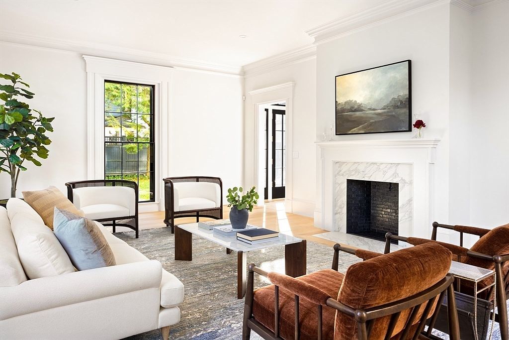 This elegant living room features a sophisticated blend of modern and classic design, anchored by a marble-surround fireplace and a large landscape painting. The space is furnished with a plush white sofa, two rich brown velvet armchairs, and two cane-back accent chairs, all arranged around a sleek marble-topped coffee table on a textured area rug. Large windows with black frames allow natural light to flood the room, creating an airy and inviting atmosphere perfect for high-end residential living.