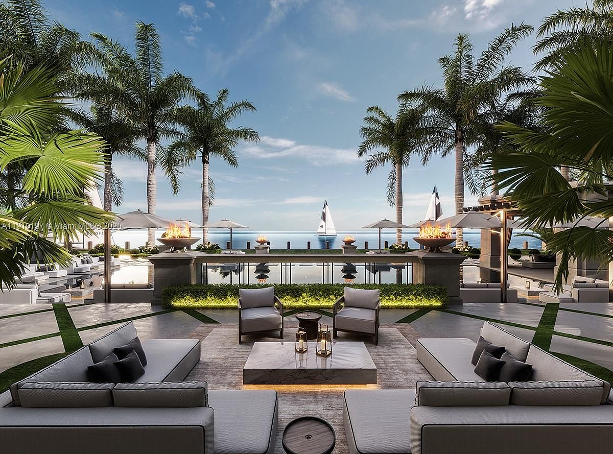 This image showcases a luxurious outdoor patio area with a stunning ocean view. The space is furnished with modern, comfortable seating arrangements, including sofas and chairs, arranged around a stylish coffee table. Palm trees frame the scene, and fire pits add a touch of elegance, creating an inviting and upscale outdoor living space perfect for relaxation and entertaining.
