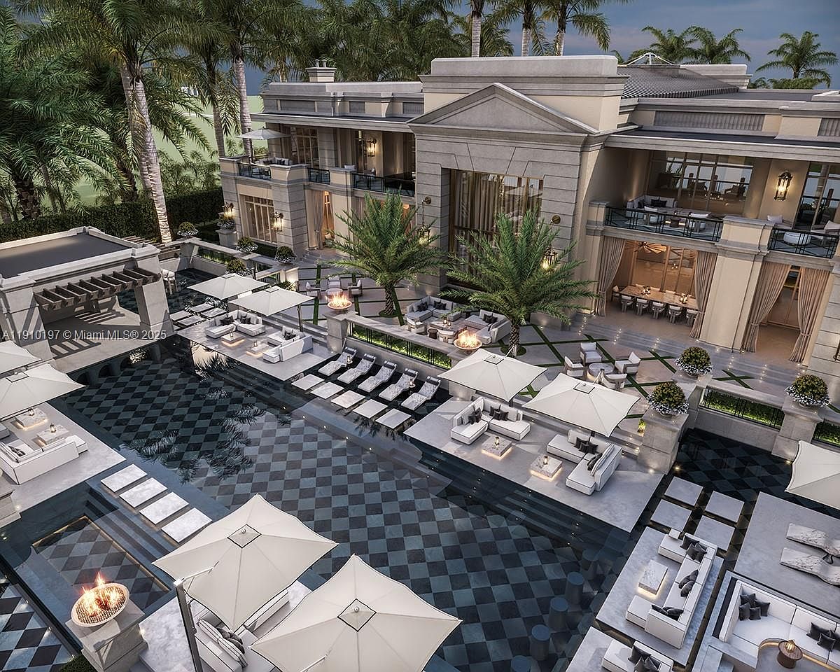 This image showcases a luxurious outdoor pool and spa area, featuring a striking checkered pattern pool design surrounded by elegant lounge seating and umbrellas. The area is complemented by lush landscaping, including palm trees, and a grand architectural building in the background, creating a resort-like ambiance perfect for relaxation and entertainment. The aerial perspective emphasizes the scale and sophistication of the property.