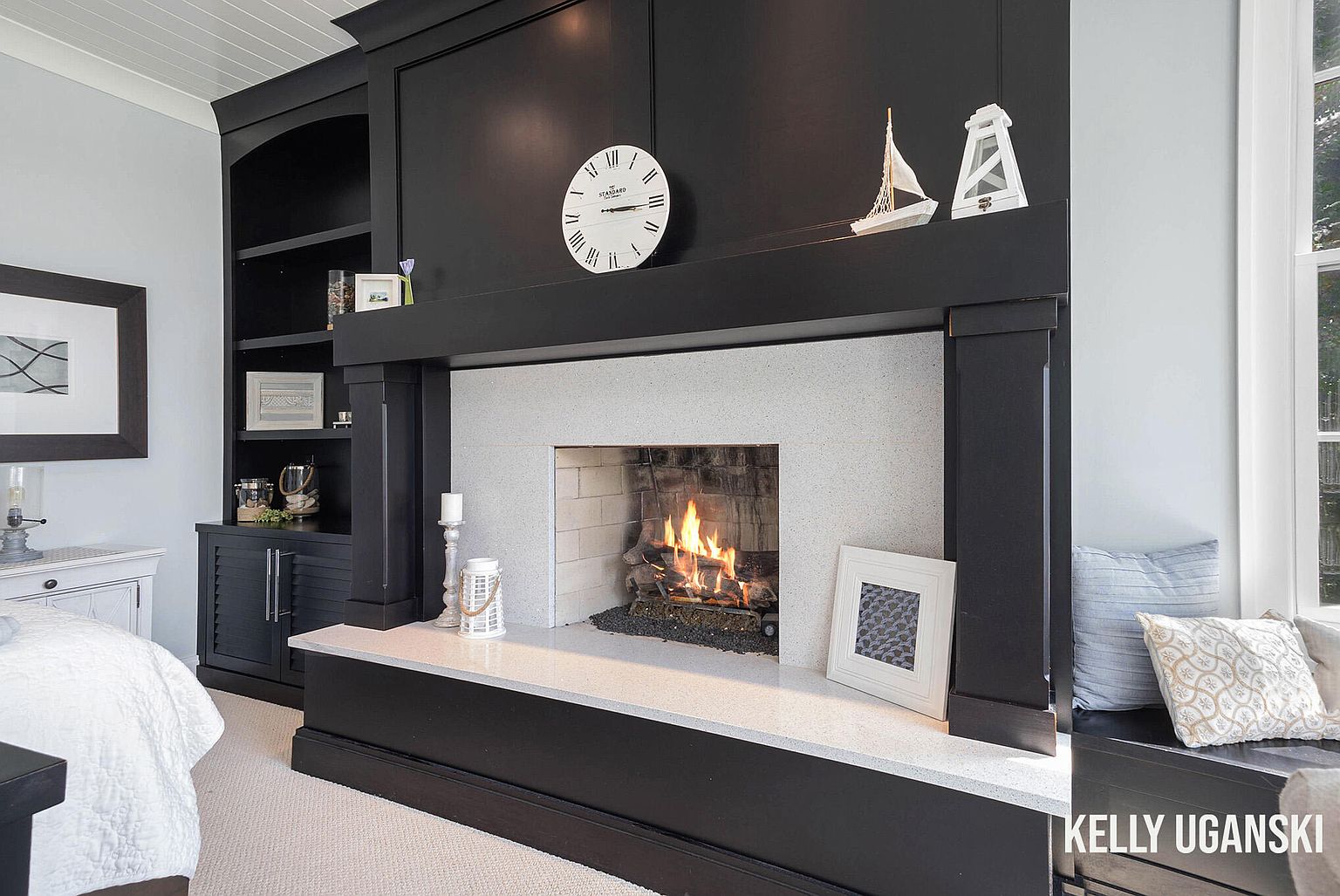 This is a cozy primary bedroom featuring a fireplace with a black surround and a light-colored hearth. Built-in black cabinetry flanks the fireplace, providing storage and display space. The room has a serene and inviting atmosphere, perfect for relaxation.