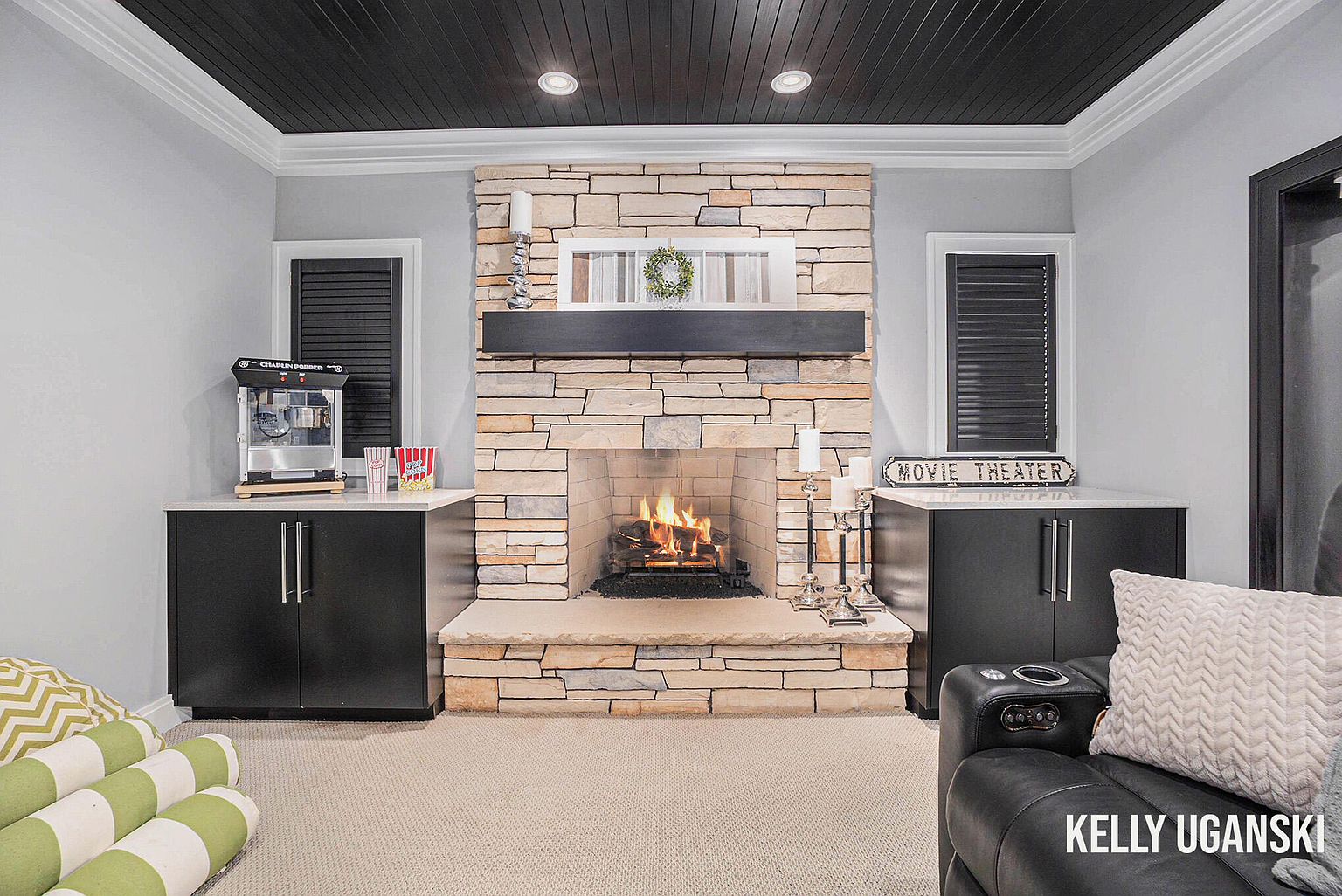 This interior shot showcases a cozy living room with a stone fireplace as the focal point. The room features built-in cabinets on either side of the fireplace, a dark wood plank ceiling, and neutral-toned walls. The overall impression is warm and inviting, suggesting a comfortable space for relaxation and entertainment.