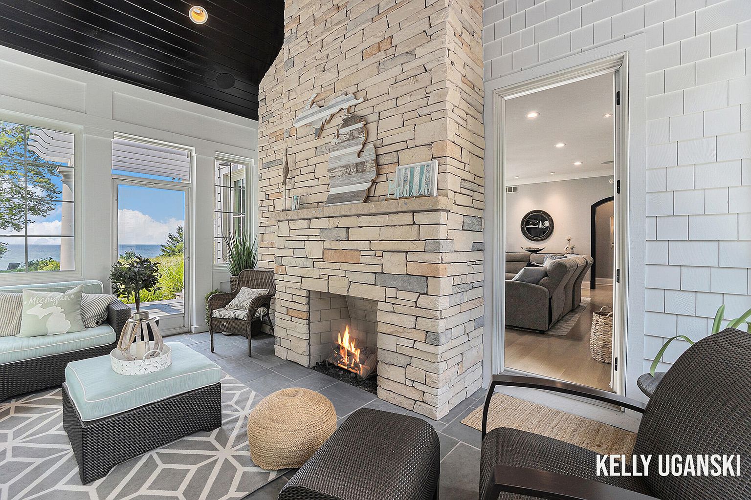 This sunroom features a stone fireplace as a focal point, complemented by wicker furniture and a geometric patterned rug. Large windows offer a view of the outdoors, creating a bright and airy atmosphere. The room provides a cozy and inviting space for relaxation and enjoying the natural surroundings.