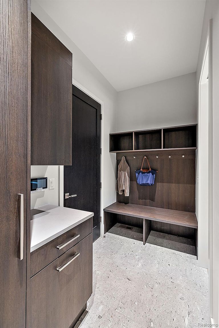 This interior shot showcases a modern hallway or entryway featuring dark wood cabinetry and a built-in bench with storage. A dark-colored door adds contrast, while the light-colored flooring and walls create a bright and airy feel. The space is well-organized and functional, perfect for a mudroom or transition area.