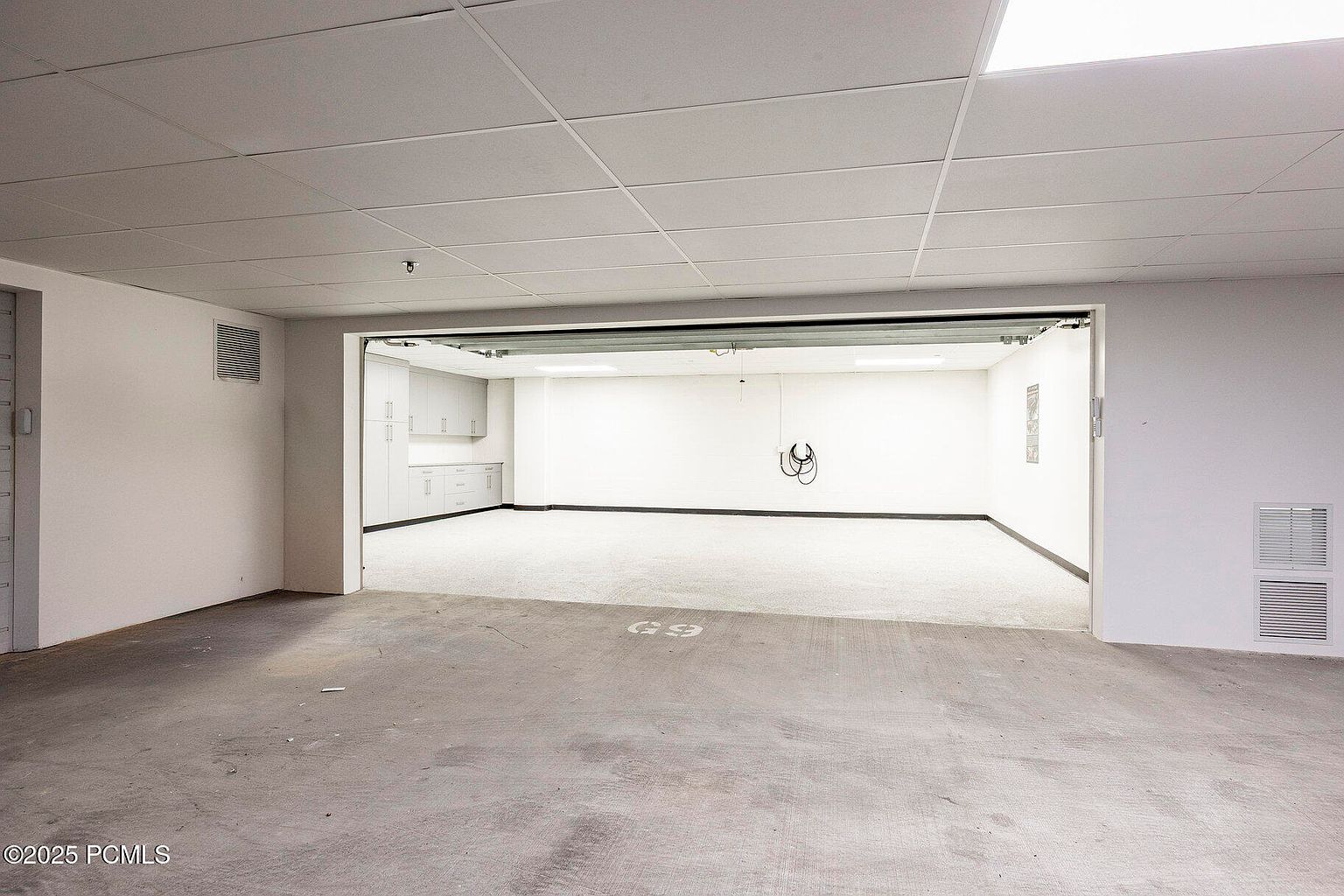 This is an interior shot of a garage. The garage features white walls, a concrete floor, and built-in cabinets. The space is well-lit and appears clean and organized, suggesting a functional and well-maintained area for parking and storage.