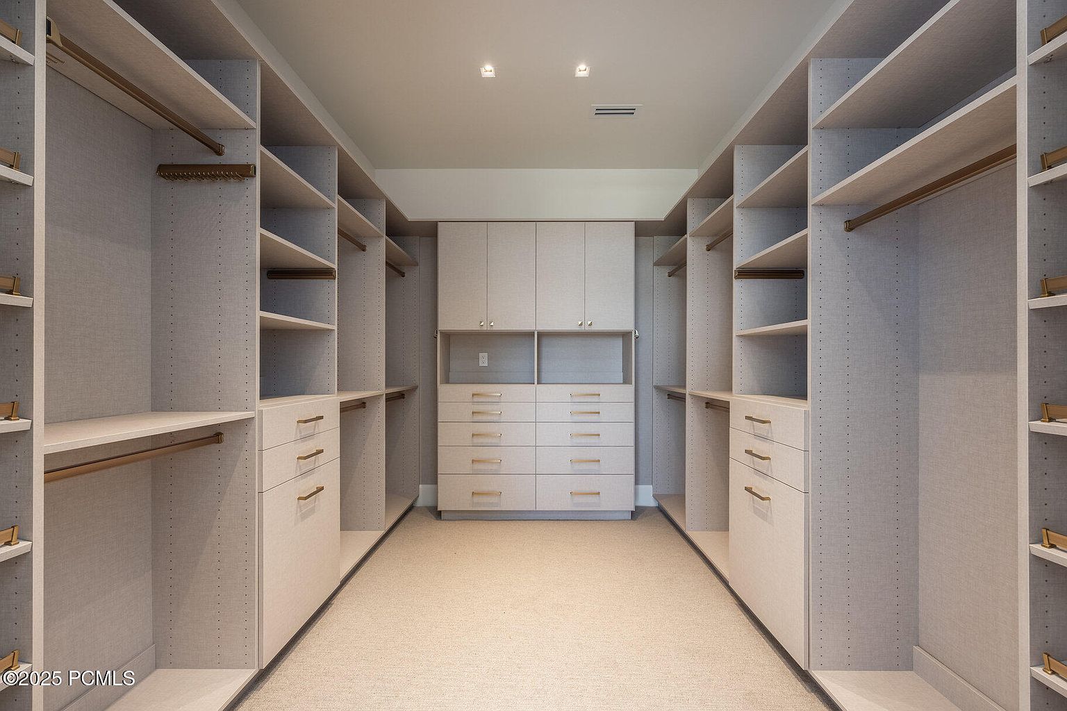 This is a well-organized walk-in closet featuring custom shelving, drawers, and hanging rods. The closet is finished in a light neutral tone, creating a clean and spacious feel. The layout maximizes storage and accessibility, making it a desirable feature for potential buyers.