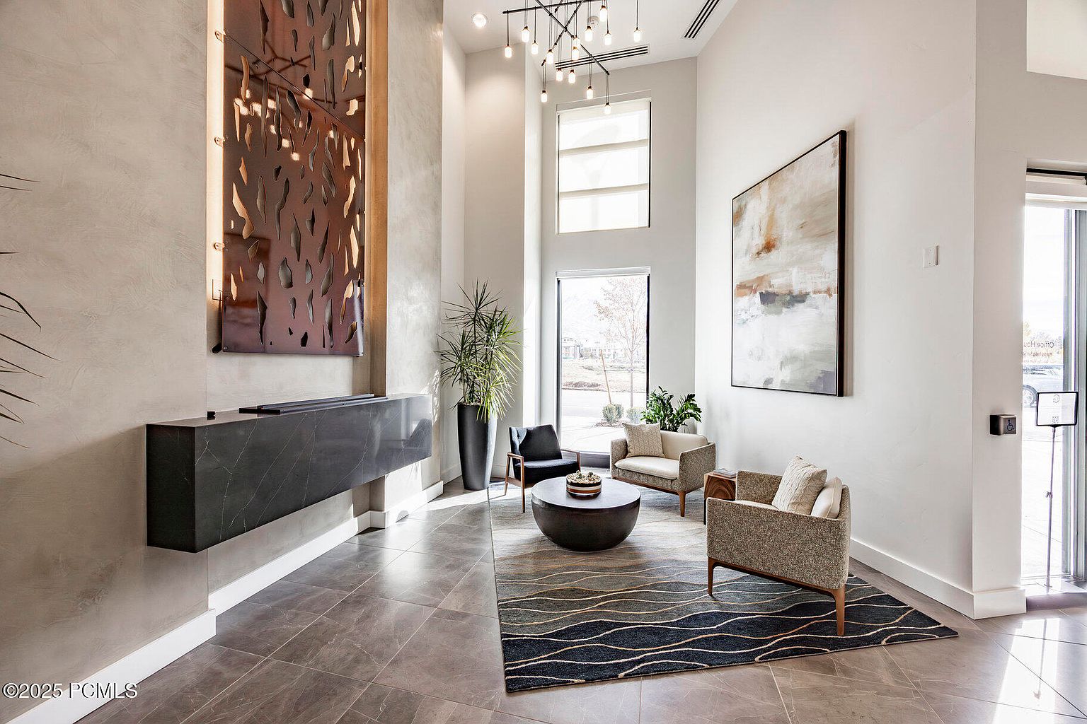 This is a shot of a modern and stylish living room area. The room features a high ceiling, a large abstract painting, and contemporary furniture including armchairs and a round coffee table. A unique metal wall art piece and a sleek, floating console add to the room's sophisticated aesthetic.