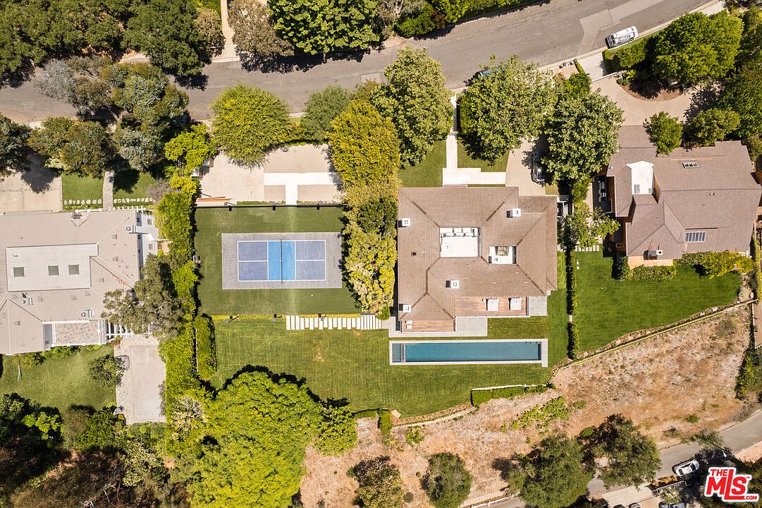 This aerial shot showcases a luxurious property featuring a large house with a brown roof, a rectangular swimming pool, and a tennis court. The manicured lawn and surrounding trees add to the estate's appeal, creating a sense of privacy and exclusivity. The image highlights the spaciousness and amenities of the property.