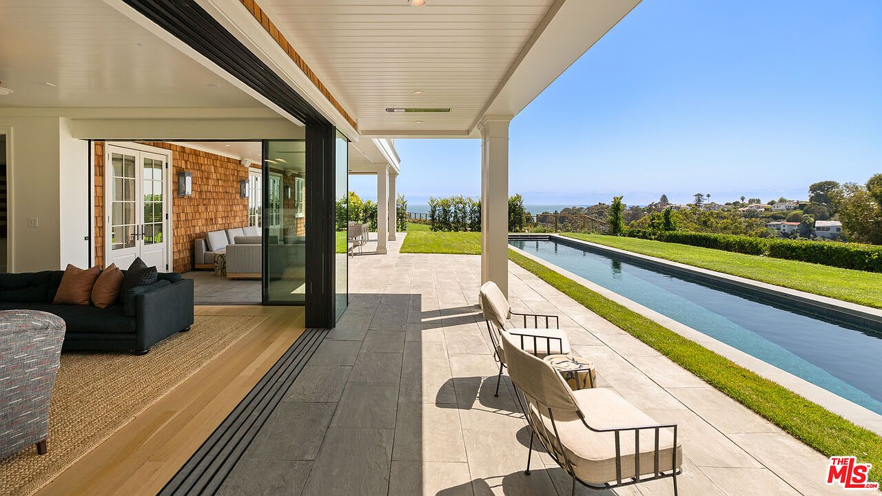 This image showcases a luxurious outdoor patio area with a stunning view. The patio features elegant seating arrangements, a long lap pool, and well-manicured landscaping. The open design seamlessly connects the indoor living space with the outdoor area, creating an inviting and relaxing atmosphere.