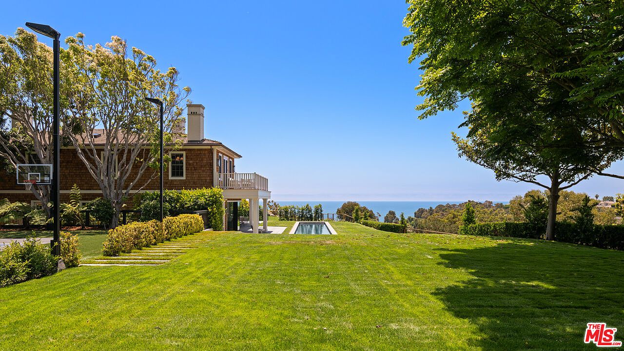 This image showcases a beautifully landscaped backyard featuring a lush green lawn, mature trees, and manicured hedges. A swimming pool is visible in the distance, offering a glimpse of the ocean beyond. The property exudes a sense of tranquility and privacy, making it an ideal outdoor space for relaxation and entertainment.