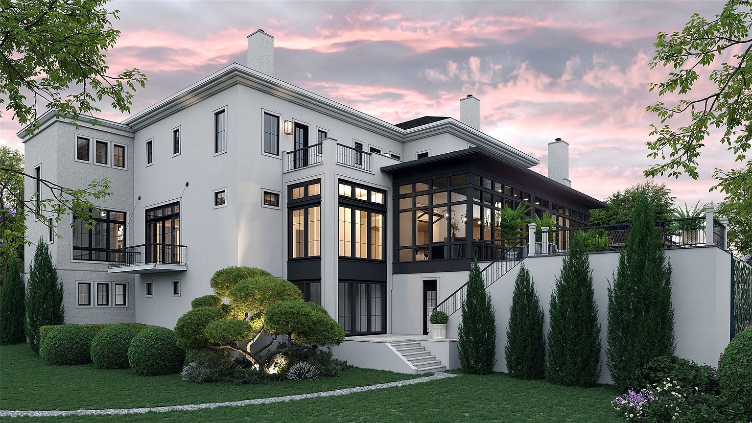 This is a rear view of a modern, multi-story home with a white stucco exterior and black-framed windows. The architecture features a combination of flat and gabled rooflines, with a sunroom/conservatory addition. The landscaped yard includes manicured bushes, trees, and a stone pathway, creating a serene and upscale ambiance.