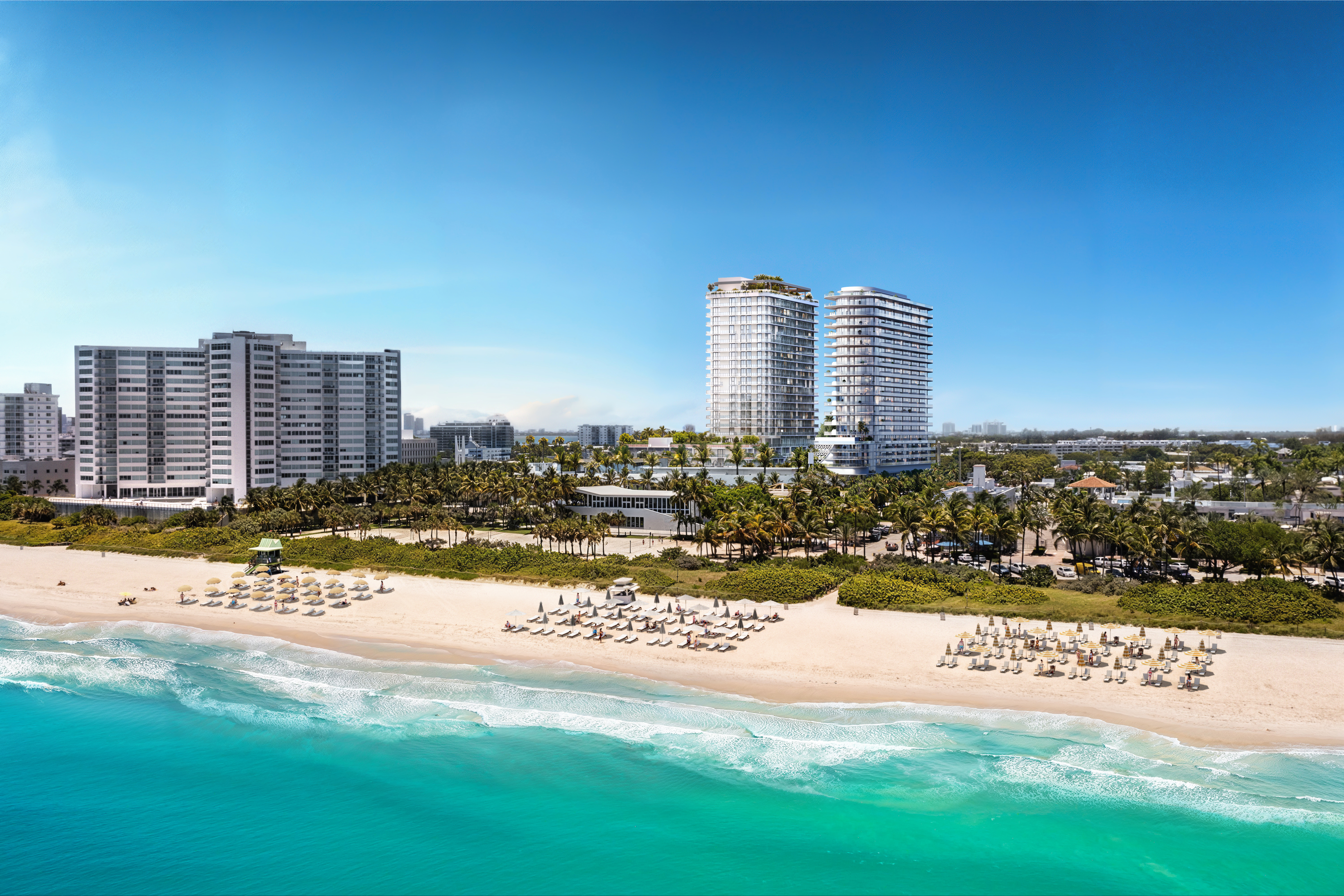 This aerial view showcases a stunning beachfront property featuring modern high-rise buildings adjacent to a pristine sandy beach and turquoise ocean. The scene includes meticulously arranged beach umbrellas and lounge chairs, lush palm trees, and clear blue skies, creating an inviting and luxurious coastal living experience. The perspective is a wide shot, capturing the scale of the buildings and the expansive beach.