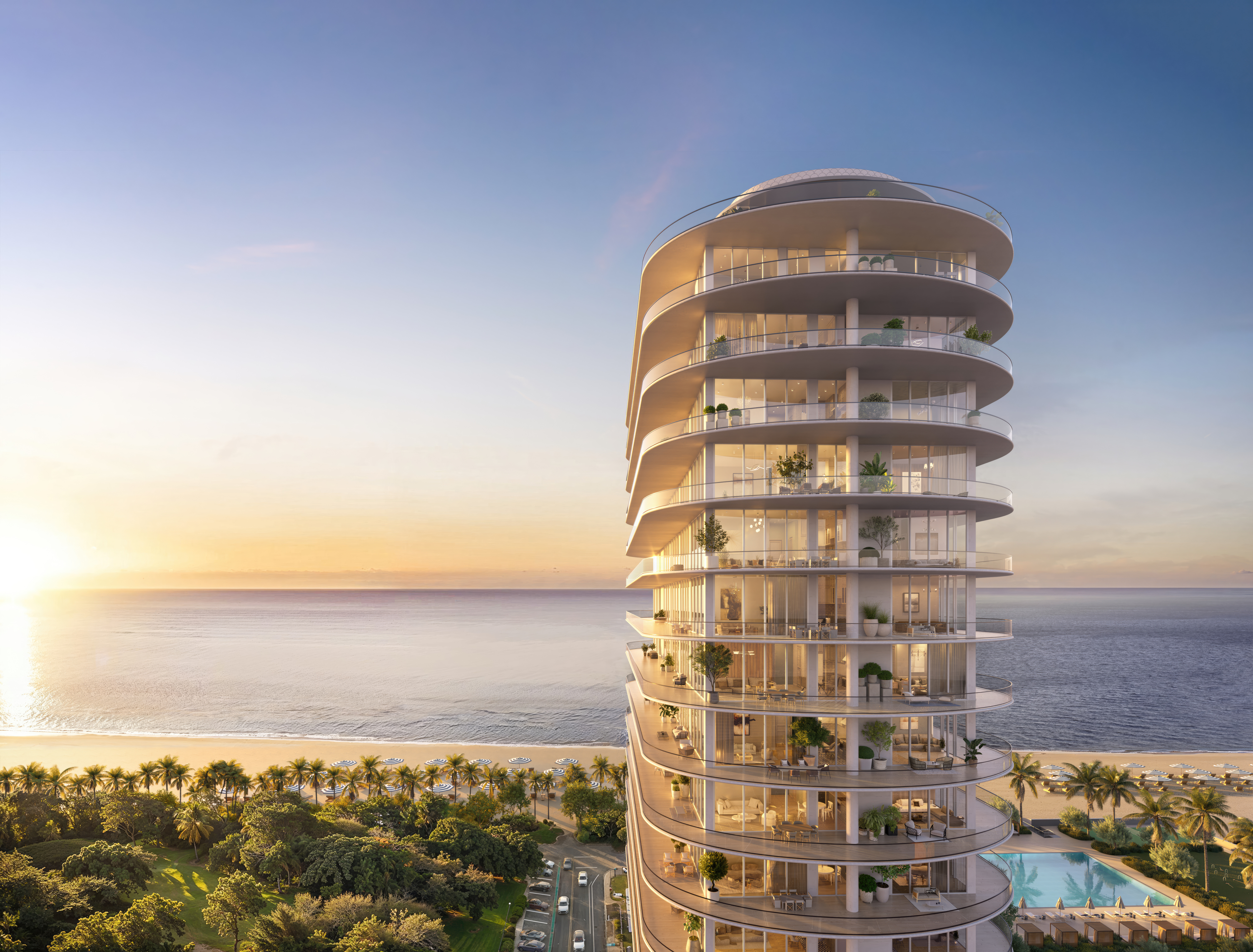 This aerial view showcases a modern, high-rise condominium building with curved balconies overlooking a pristine beach and ocean. The building is situated next to lush greenery, a swimming pool, and a road with cars, offering a blend of urban and natural environments. The overall impression is luxurious and serene, highlighting the property's prime location and upscale amenities.