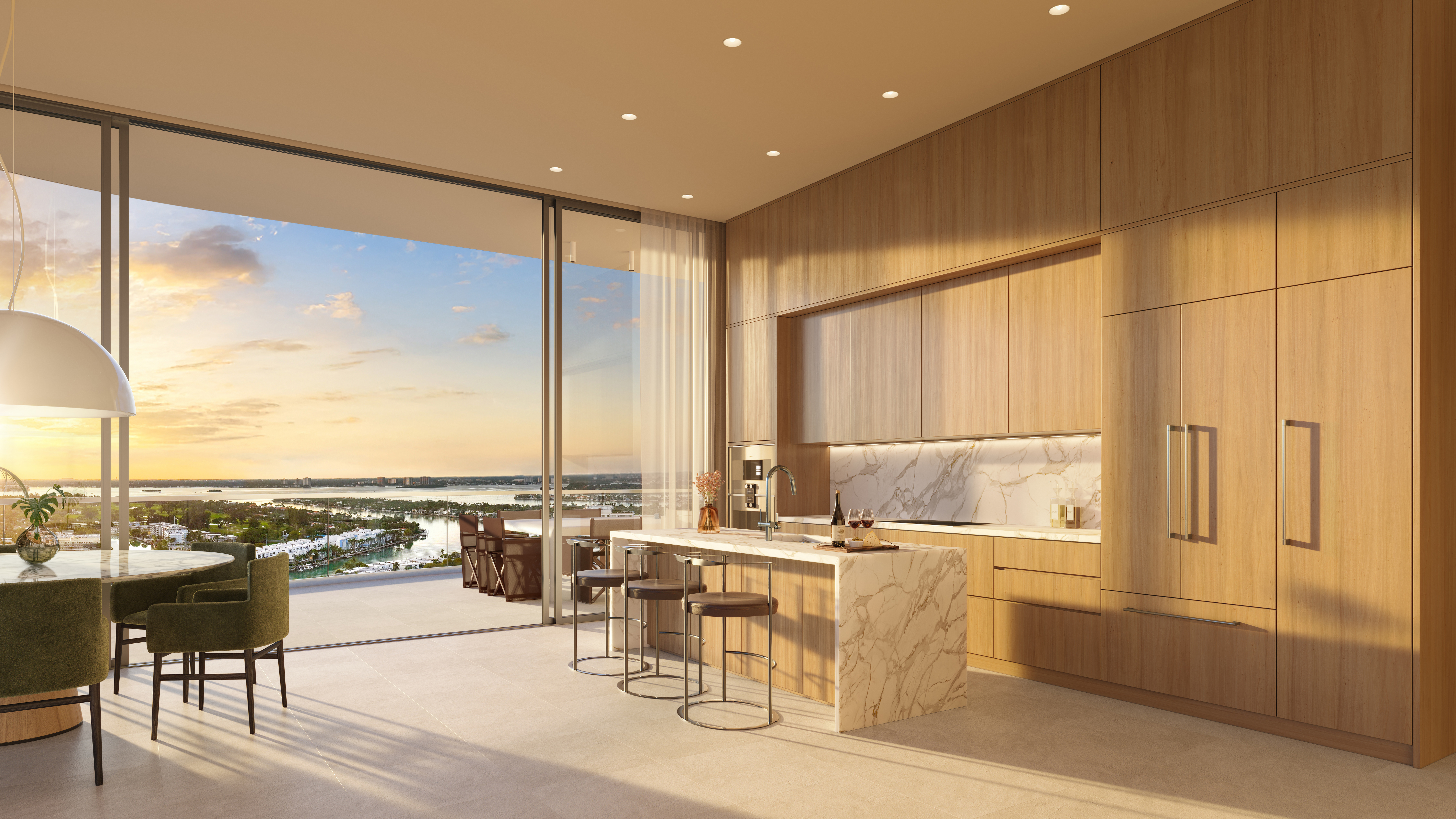 This is a bright and modern kitchen with sleek, light wood cabinetry and a marble-topped island with seating. Large sliding glass doors open to a balcony with a stunning sunset view, seamlessly blending indoor and outdoor living. The kitchen is well-appointed and exudes a sense of luxury and sophistication.