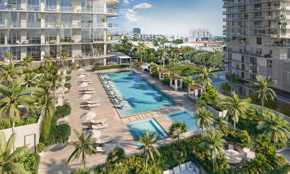 This aerial view showcases a luxurious pool and spa area nestled between modern high-rise buildings. The pool is surrounded by lounge chairs and umbrellas, with lush landscaping and palm trees adding to the tropical ambiance. The scene evokes a sense of relaxation and upscale living.
