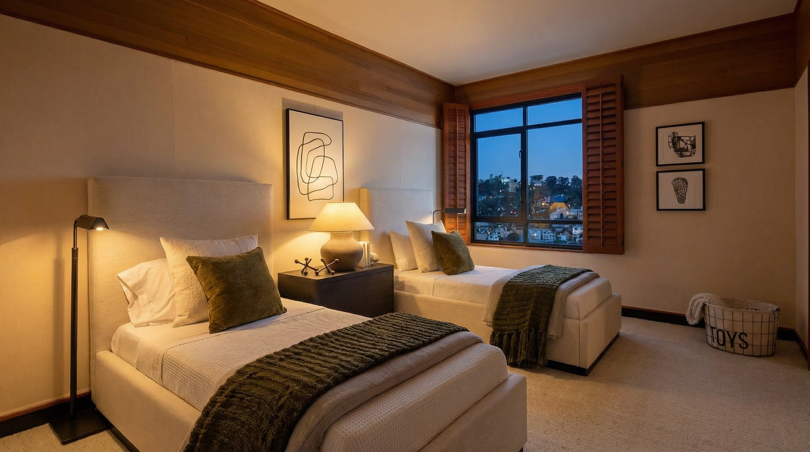 This bedroom features two twin beds with white linens and olive green accents, creating a serene and inviting atmosphere. A wooden ceiling trim adds warmth, while artwork and a window with a view enhance the room's appeal. The perspective is from the foot of one of the beds, showcasing the layout and design elements.