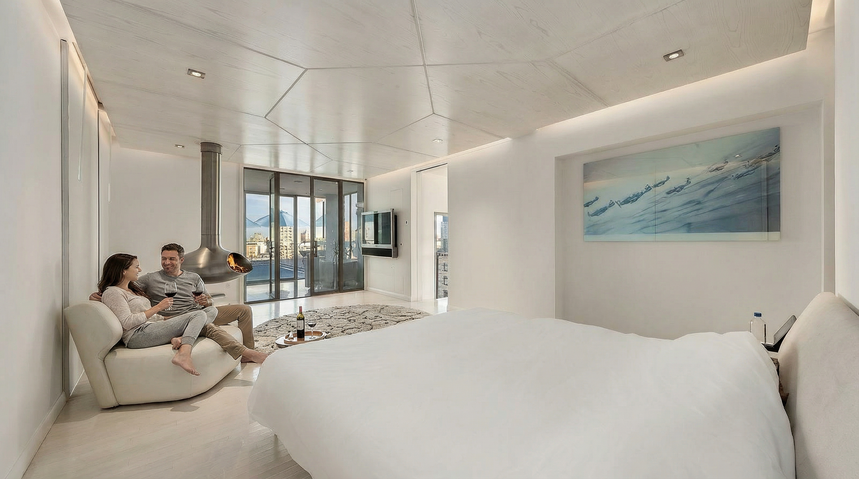 This ultra-modern primary bedroom features a minimalist aesthetic with a striking geometric wood-paneled ceiling and a suspended, sculptural fireplace. A plush white lounge chair sits near a large glass door that opens to a balcony, while a serene abstract painting hangs above the bed. The room is bathed in soft, ambient lighting, creating a sophisticated and tranquil atmosphere.