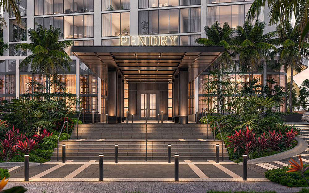 This image showcases the grand entryway of a modern building, likely a luxury residence or hotel, featuring a covered entrance with the name "PENDRY" prominently displayed. The entrance is accessed by a wide set of stairs flanked by lush tropical landscaping, including palm trees and vibrant red foliage, creating an inviting and upscale atmosphere. The scene is illuminated by subtle lighting, enhancing the architectural details and highlighting the manicured surroundings.