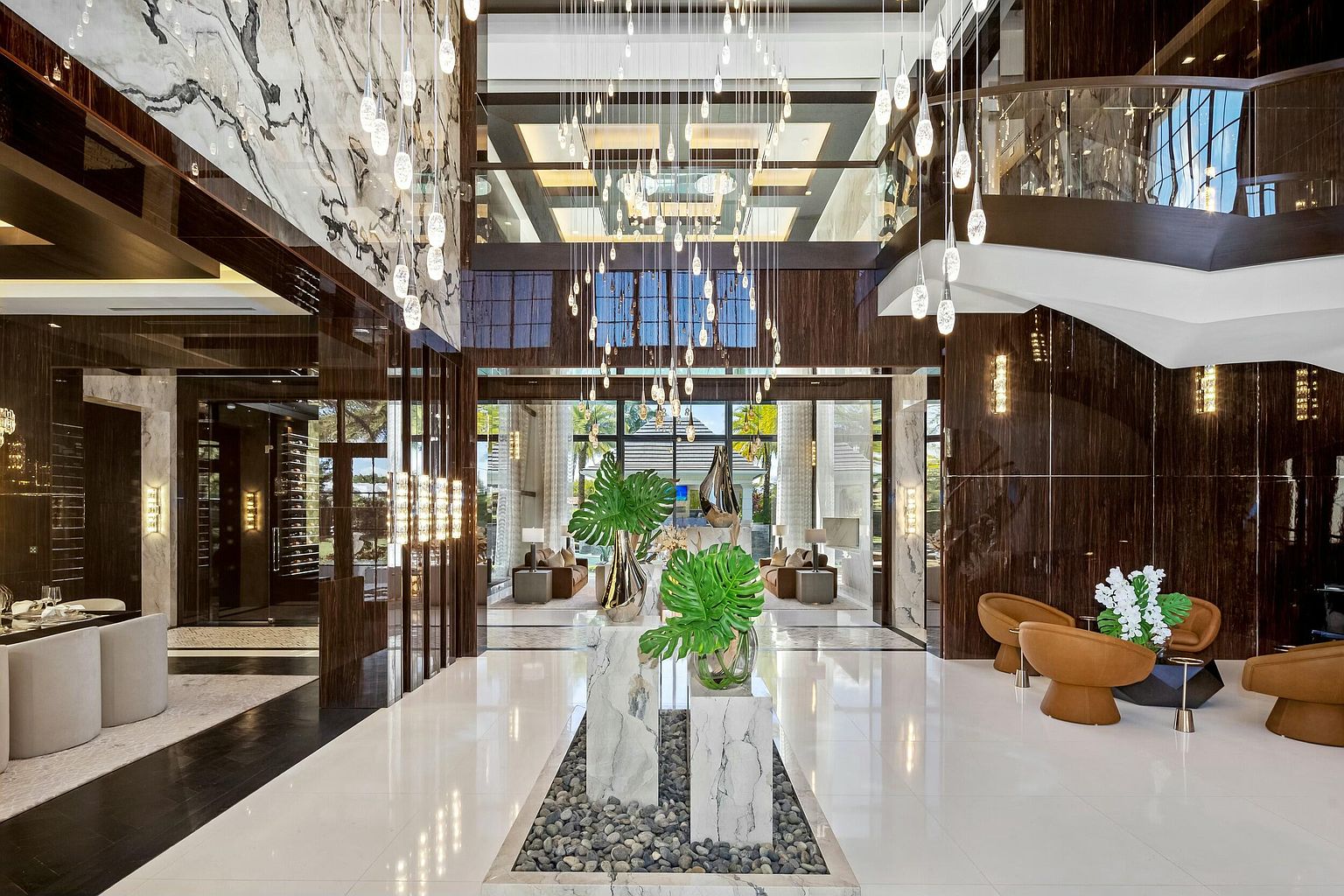 This grand foyer features soaring ceilings, a striking chandelier, and elegant marble and wood finishes. The open layout leads to various living spaces, creating a sense of luxury and spaciousness. The design incorporates modern elements with a focus on natural light and sophisticated details.