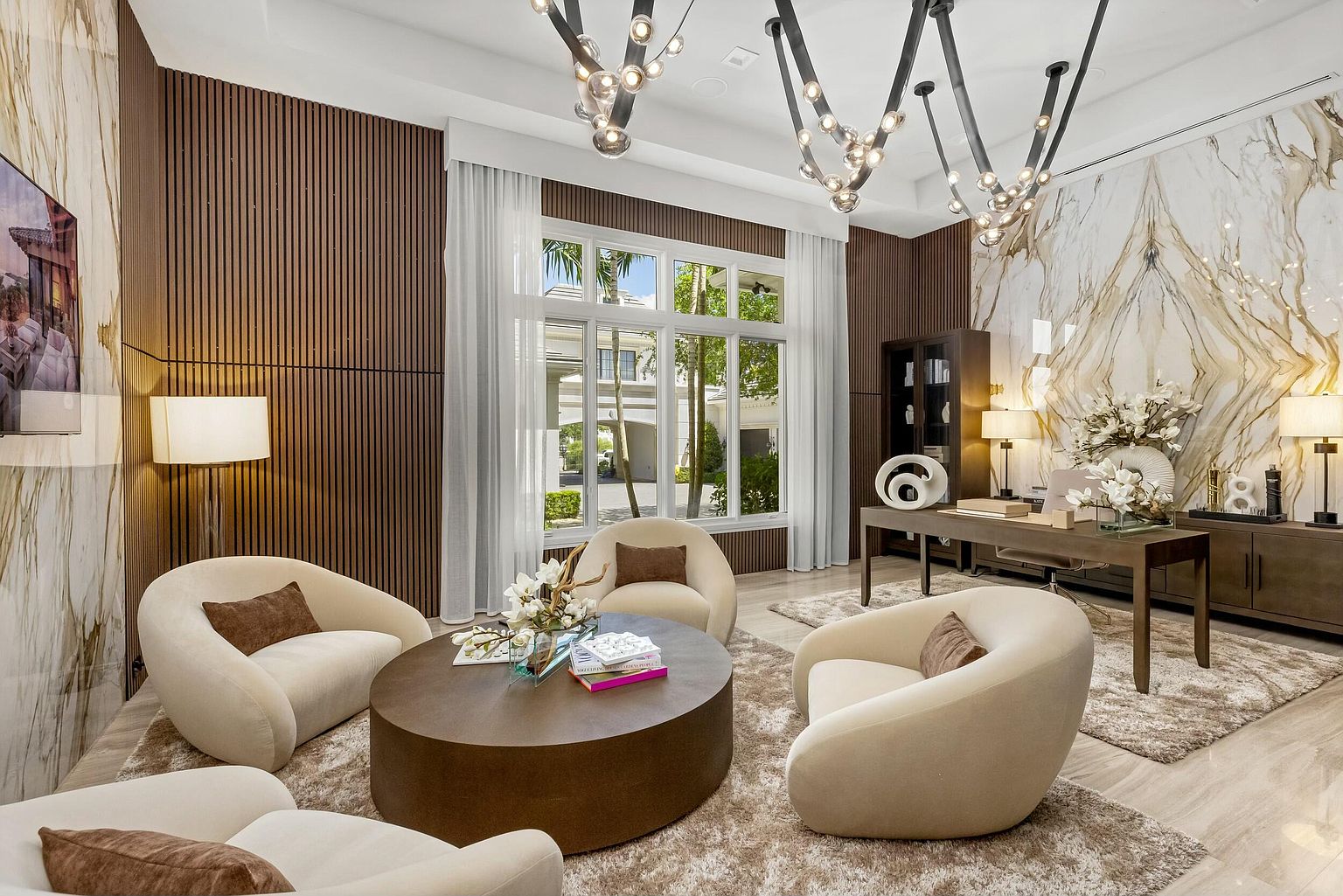 This interior shot showcases a luxurious living room with a modern design. The room features a unique lighting fixture, comfortable rounded chairs, and a stylish coffee table, all set on a plush rug. The walls are adorned with a combination of wood paneling and marble, creating a sophisticated and inviting atmosphere.