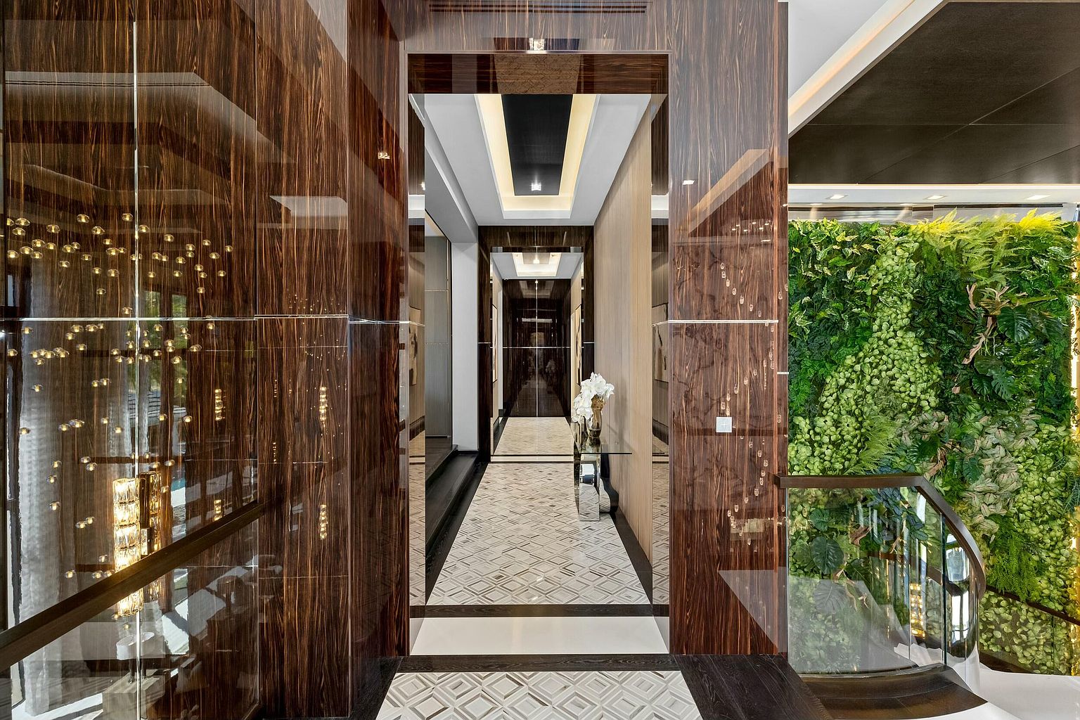 This interior shot showcases a luxurious hallway with a striking geometric tile floor and rich wood-paneled walls. The hallway leads to a bright, naturally lit area with a vertical garden, creating a blend of modern elegance and natural elements. The design emphasizes depth and sophistication, making it a memorable feature of the property.
