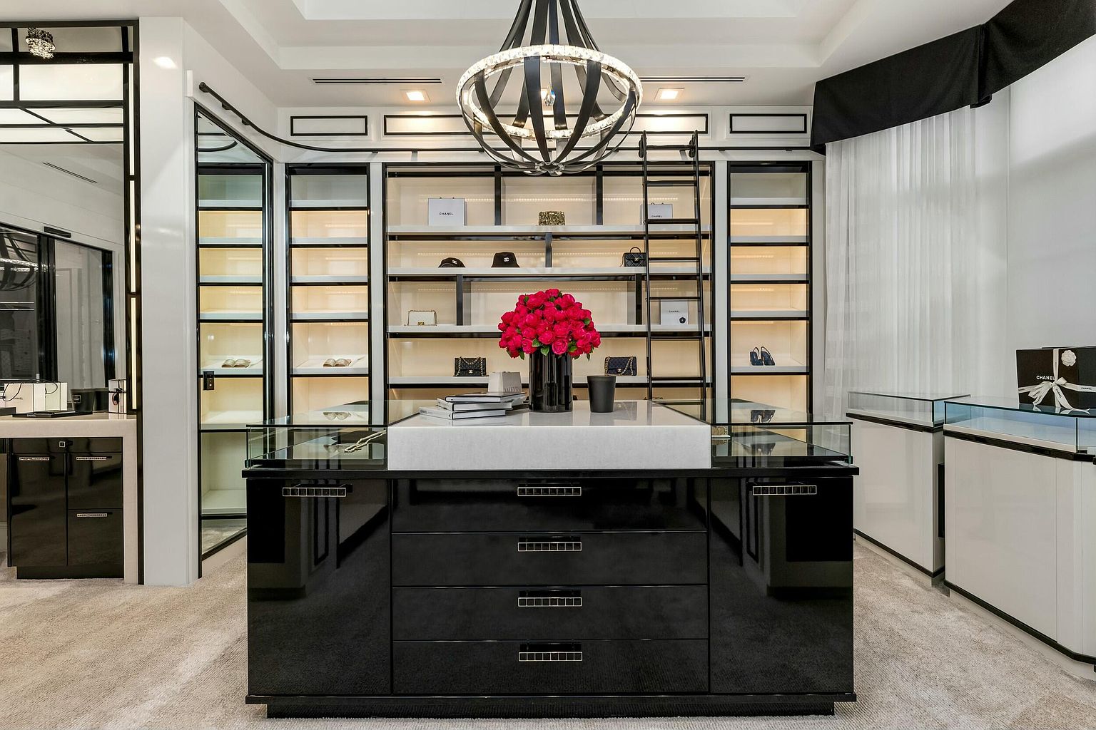 This is a luxurious walk-in closet featuring custom shelving with integrated lighting, displaying handbags and accessories. A central island with a marble countertop and black cabinetry provides additional storage and display space. The overall design is modern and high-end, creating an aspirational space for organization and style.