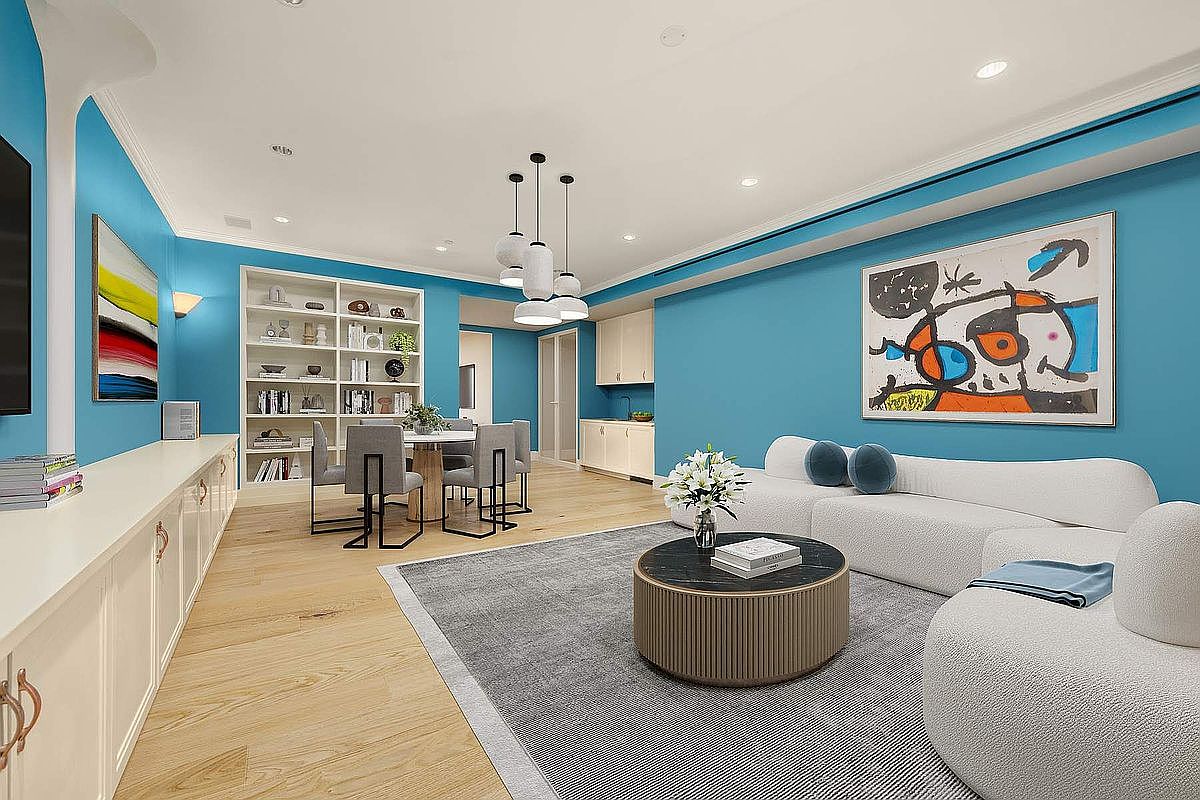 This vibrant living and dining area features bold turquoise walls contrasted by a sleek, curved white sofa and light wood flooring. The space is anchored by a large, abstract art piece and a modern circular coffee table, creating a sophisticated and contemporary atmosphere. The open-concept layout flows seamlessly into a dining nook with built-in shelving, illuminated by stylish pendant lighting.