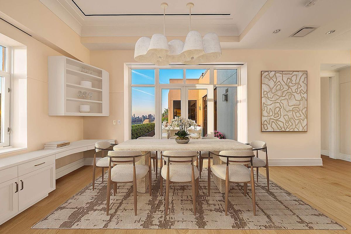 This elegant dining room features a sophisticated, neutral color palette with light cream walls and a textured area rug anchoring the space. A modern, sculptural chandelier hangs above a substantial stone-topped dining table surrounded by six upholstered chairs, while a built-in white shelving unit provides refined storage. Large glass doors open to a terrace, inviting natural light and offering a scenic view of the city skyline beyond.