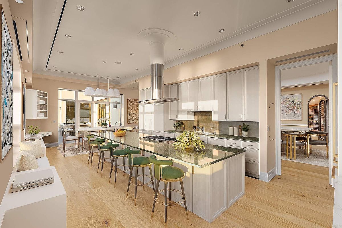 This sophisticated, open-concept kitchen features a large central island with a dark stone countertop and elegant green velvet bar stools, serving as the focal point of the room. The space is brightened by recessed lighting and a series of modern pendant lights, complemented by light-toned hardwood flooring and cream-colored cabinetry. The perspective captures the seamless flow from the kitchen into the adjacent dining area, highlighting a luxurious and airy atmosphere perfect for entertaining.