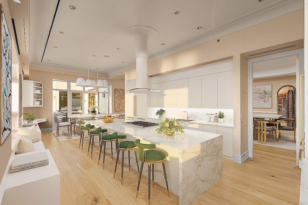 This sophisticated, open-concept kitchen features a massive marble-topped island with elegant green velvet bar stools, serving as the centerpiece of the room. The space is defined by sleek, minimalist white cabinetry, high-end integrated appliances, and warm hardwood flooring that creates a bright, airy atmosphere. A cinematic wide-angle perspective captures the seamless flow from the kitchen into the adjacent dining area and outdoor patio, highlighting a luxurious and modern design aesthetic.