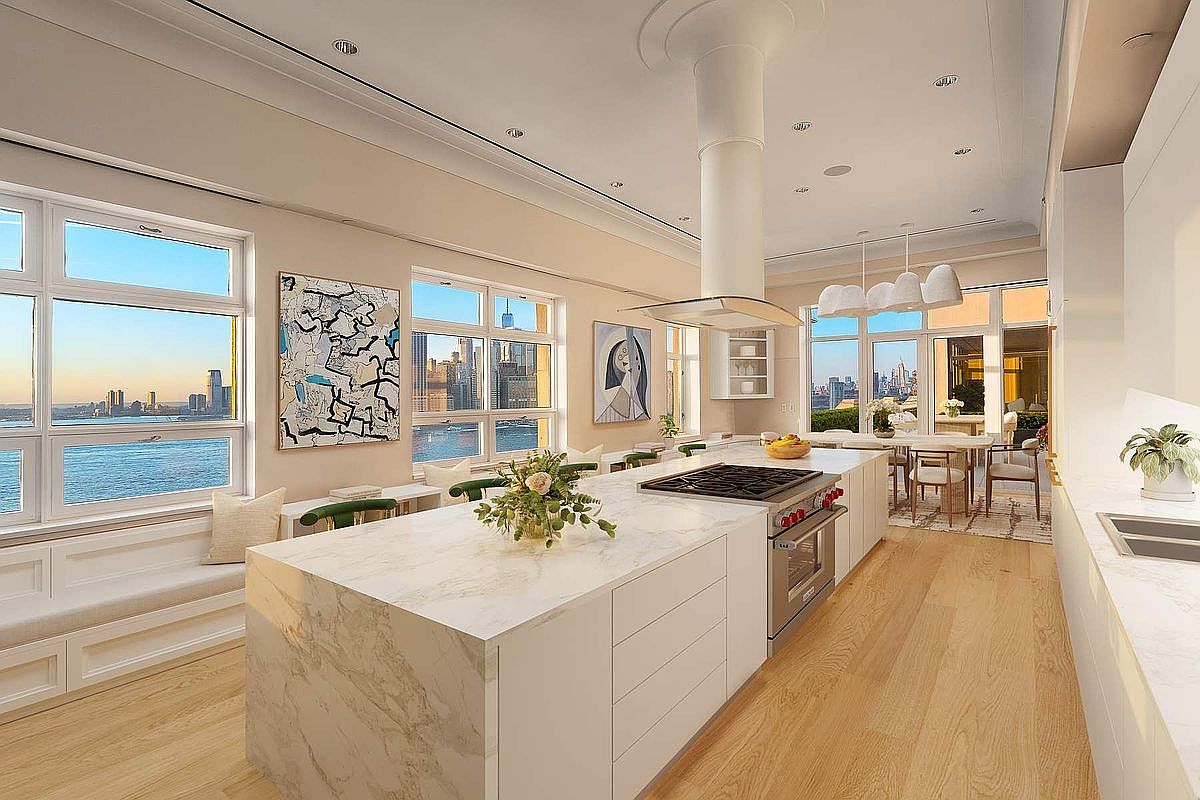 This sophisticated, modern kitchen features a massive waterfall-edge marble island, sleek white cabinetry, and high-end stainless steel appliances. The open-concept space is bathed in natural light from floor-to-ceiling windows that offer breathtaking panoramic views of the city skyline and waterfront. The minimalist design, accented by contemporary art and elegant pendant lighting, creates an airy and luxurious atmosphere perfect for high-end urban living.