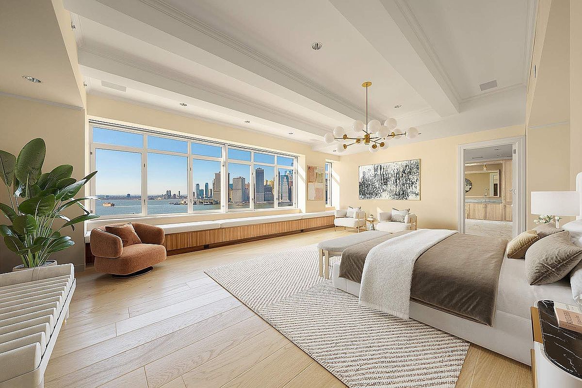 This luxurious primary bedroom features a sophisticated, neutral color palette and expansive floor-to-ceiling windows that offer a stunning panoramic view of the city skyline and waterfront. The room is anchored by a plush bed with high-end linens, complemented by a modern chandelier, a cozy accent chair, and a long built-in window bench. The light wood flooring and clean architectural lines create an airy, serene, and high-end atmosphere perfect for a premium real estate listing.