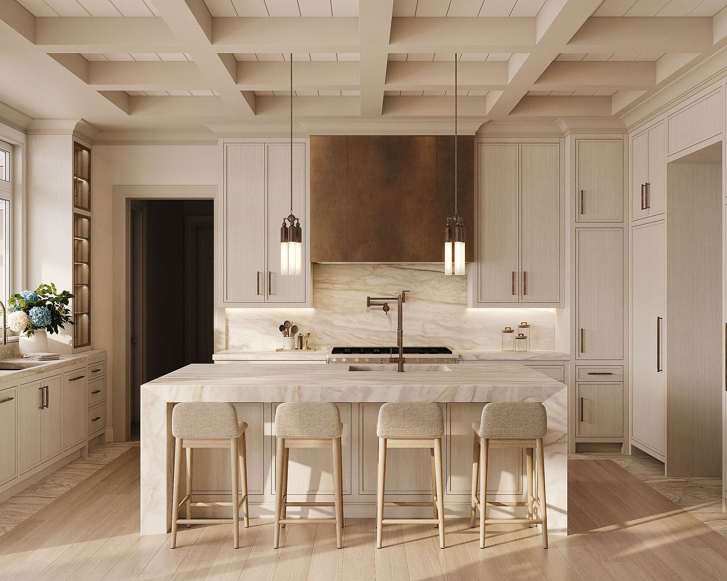 This sophisticated kitchen features a large central island with a waterfall-edge stone countertop and four light-toned stools. The space is defined by light wood cabinetry, a prominent metallic range hood, and a coffered ceiling that adds architectural depth. Two elegant pendant lights hang over the island, illuminating the workspace and highlighting the clean, neutral aesthetic of the room.