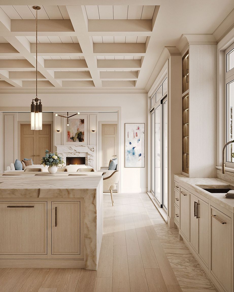This sophisticated kitchen features a large central island with a stone waterfall edge and light wood cabinetry. The space is defined by a coffered ceiling and a seamless transition into an adjacent living area, which showcases a stone-clad fireplace surround. Large glass doors allow natural light to flood the room, highlighting the neutral color palette and elegant, airy design.