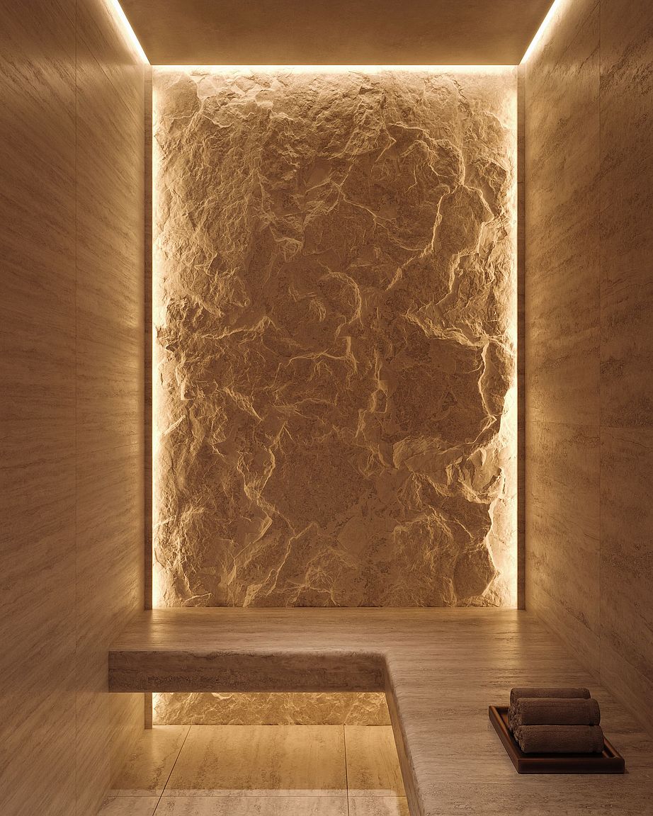 This luxurious spa-inspired space features a dramatic, textured stone accent wall illuminated by integrated perimeter lighting. A sleek, light-toned stone bench extends across the room, providing a minimalist seating area with a small tray of rolled towels. The perspective is centered and symmetrical, emphasizing the high-end, tranquil atmosphere of this wellness-focused retreat.