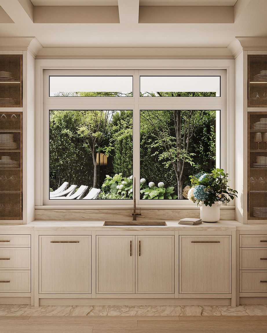 This elegant kitchen space features light wood cabinetry with integrated mesh-fronted storage flanking a central window. A stone countertop houses a sleek, dark-toned sink and faucet, positioned directly beneath a large window that provides a serene view of a lush, green garden. The composition is symmetrical and balanced, emphasizing a clean, sophisticated aesthetic with natural textures and soft, ambient lighting.