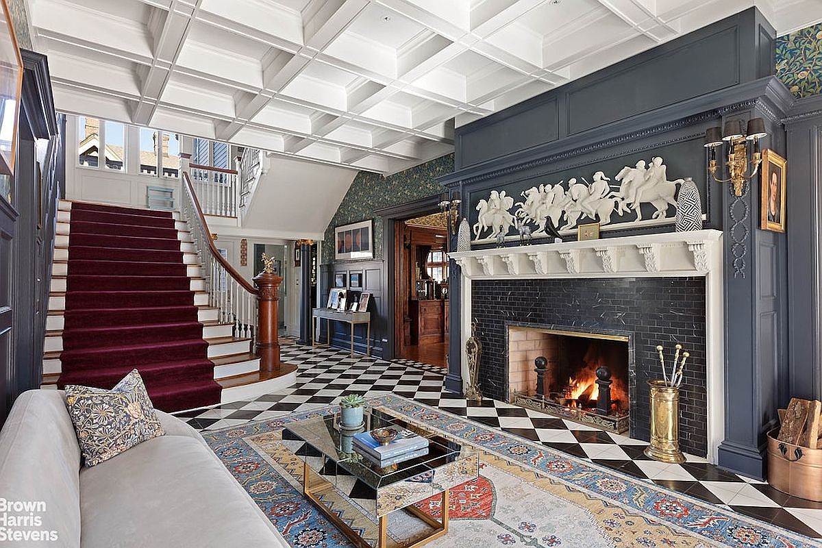 This interior shot showcases a luxurious living room with a grand fireplace, coffered ceilings, and a striking black and white checkered floor. A plush sofa and ornate rug add to the room's elegance, while a staircase leads to the upper levels, creating a sense of spaciousness and sophistication. The room exudes a classic, high-end aesthetic.