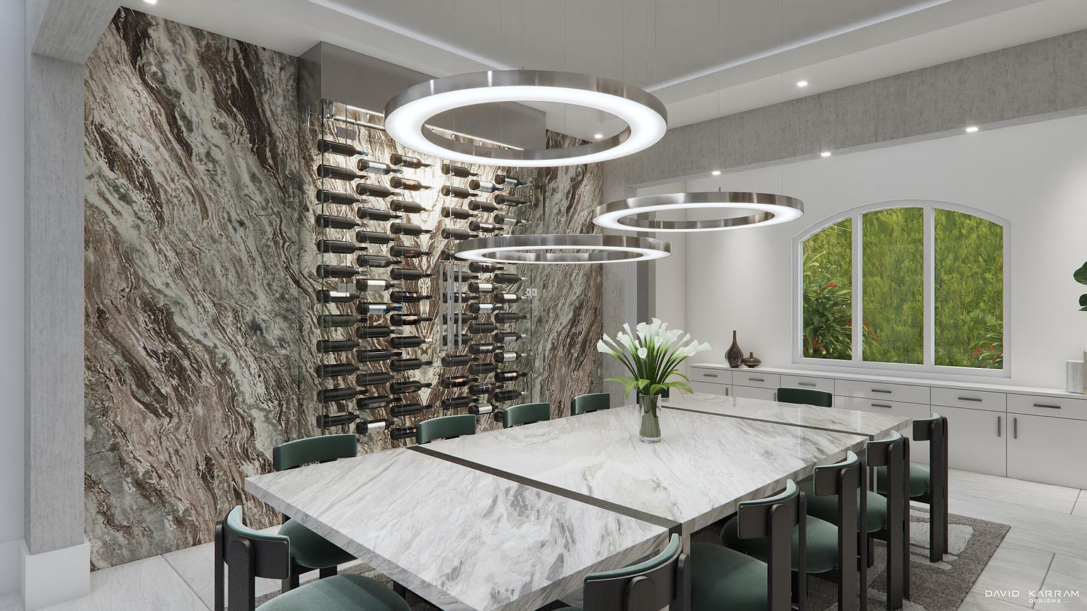 This is a modern dining room featuring a large marble table with seating for eight, illuminated by three circular pendant lights. A wine rack is built into a marble accent wall, adding a touch of luxury. A large window provides natural light and a view of the outdoors, while white cabinets line the wall opposite the wine rack.