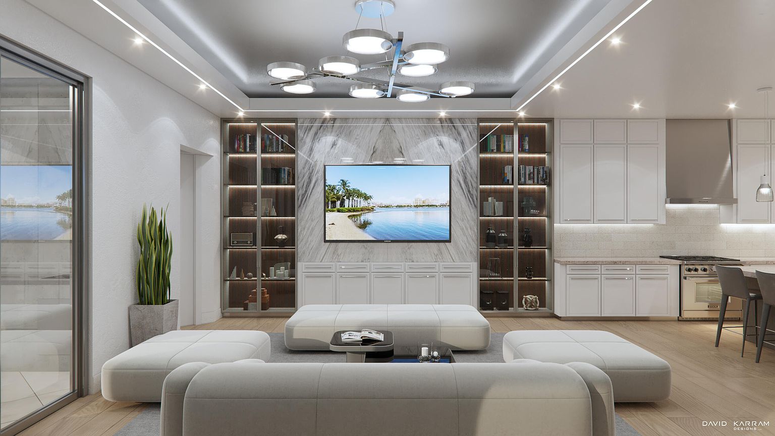 This is a modern living room featuring a large flat-screen TV mounted above a white cabinet, flanked by built-in bookshelves with decorative items. The room is furnished with white sofas and ottomans, creating a bright and airy atmosphere. The perspective is from the back of the living room, showcasing the open-concept design that integrates the living space with the kitchen area.