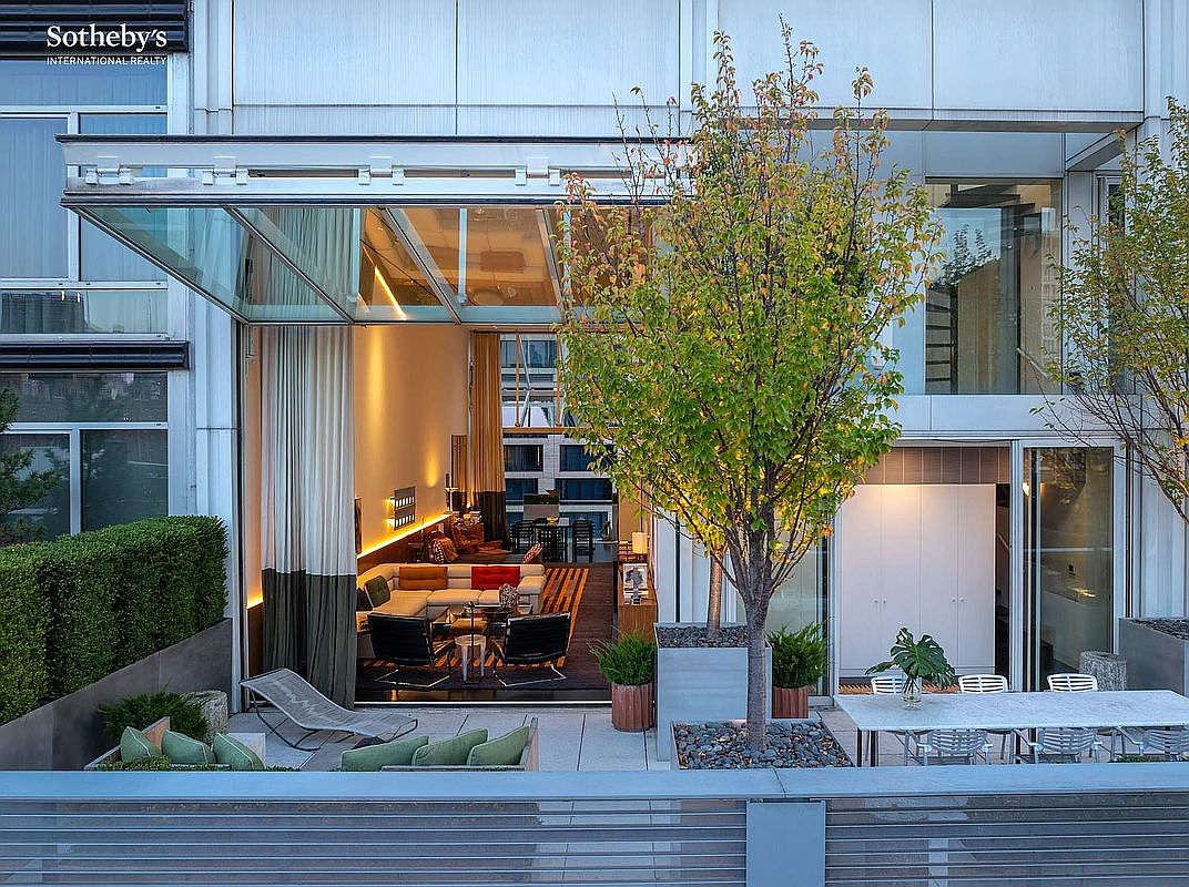 This sophisticated urban terrace features a seamless transition between an indoor living area and an outdoor lounge space, highlighted by a retractable glass wall. The deck is furnished with modern seating, a dining table, and manicured greenery, creating a luxurious and private atmosphere. The architectural design emphasizes clean lines and a contemporary aesthetic, perfect for high-end city living.