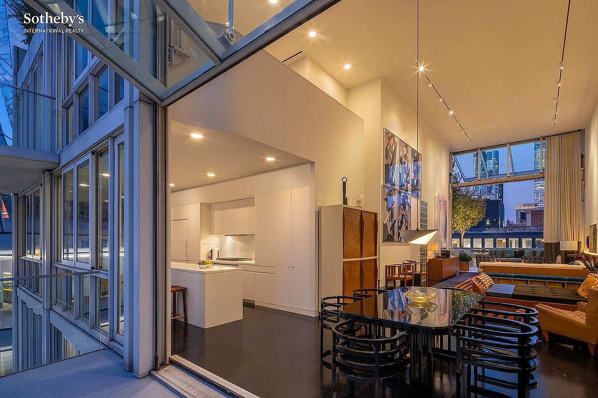 This sophisticated, open-concept living and dining area features soaring ceilings and floor-to-ceiling glass walls that seamlessly blend the interior with an expansive outdoor terrace. The space is defined by a sleek, modern aesthetic, highlighted by a glossy dark floor, contemporary black dining chairs, and a minimalist white kitchen visible in the background. The dramatic lighting and urban skyline view through the glass create a luxurious, high-end atmosphere perfect for entertaining.