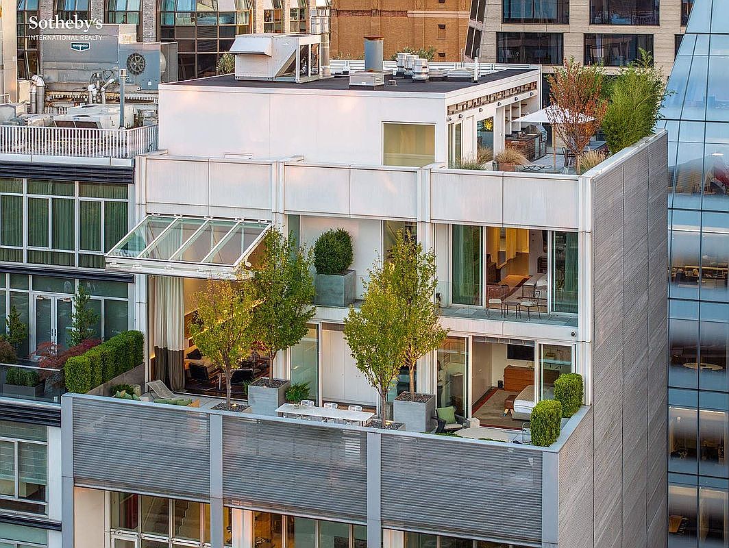 This high-angle aerial view captures a sophisticated urban penthouse terrace featuring multiple levels of outdoor living space, lush greenery, and modern architectural design. The scene highlights a seamless transition between indoor and outdoor areas, with glass-walled rooms opening onto private decks equipped with dining furniture and potted trees. The overall impression is one of luxury and exclusivity, showcasing a prime city residence with significant private outdoor amenities.