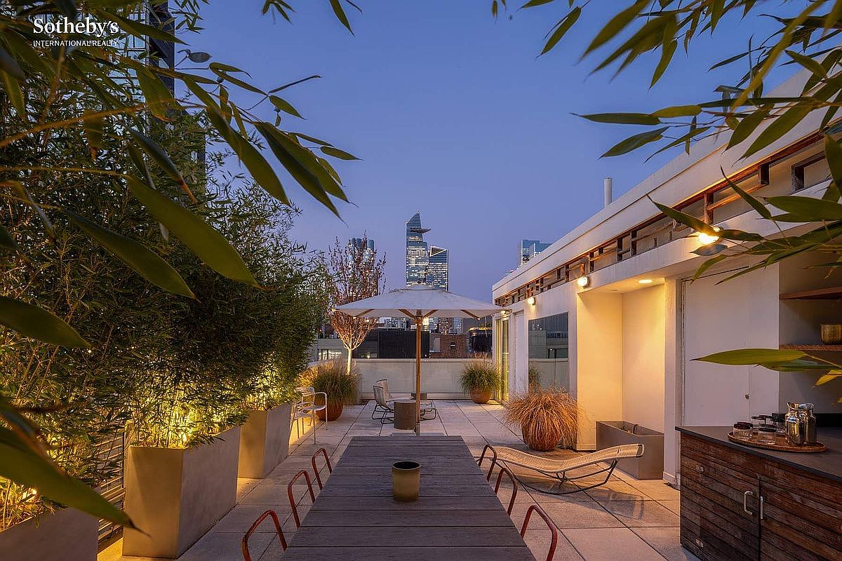 This sophisticated rooftop terrace offers a stunning urban oasis with panoramic views of the city skyline, including iconic skyscrapers. The space is thoughtfully designed with a long wooden dining table, comfortable lounge seating, and lush bamboo planters that provide both privacy and a natural aesthetic. Warm, integrated lighting creates an inviting atmosphere, making it an ideal setting for evening entertaining or relaxing outdoors.