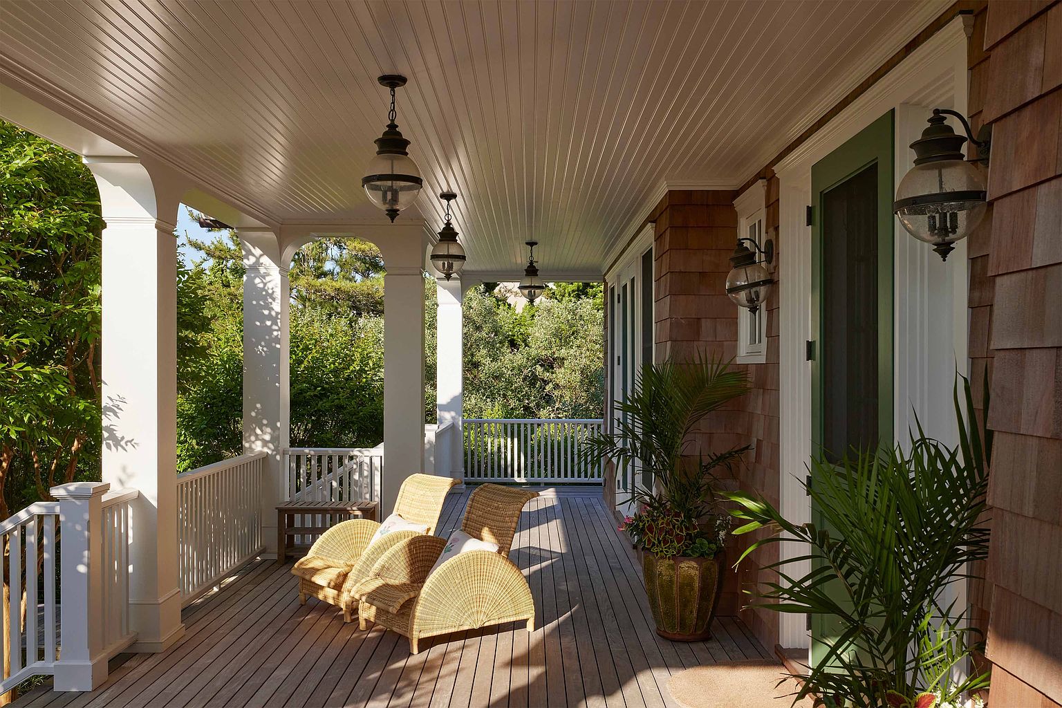 This image showcases a charming outdoor patio or deck area. The space features comfortable wicker chairs, a wooden deck, and overhead lighting, creating a cozy and inviting atmosphere. The surrounding greenery adds a touch of nature and privacy, enhancing the appeal of this outdoor living space.