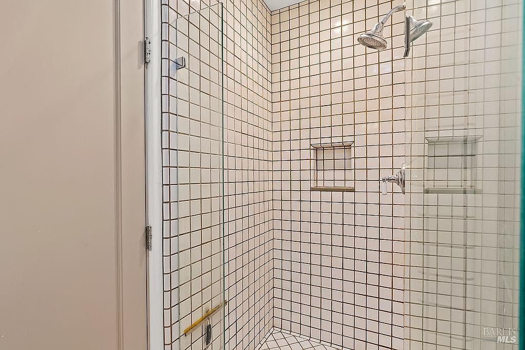 This shower enclosure features a classic grid-patterned tile design on the walls, complemented by a matching tiled floor. A glass door provides entry, while a built-in recessed niche offers convenient storage for toiletries. The shower head and control fixtures are finished in a polished metallic tone, creating a clean and functional aesthetic.