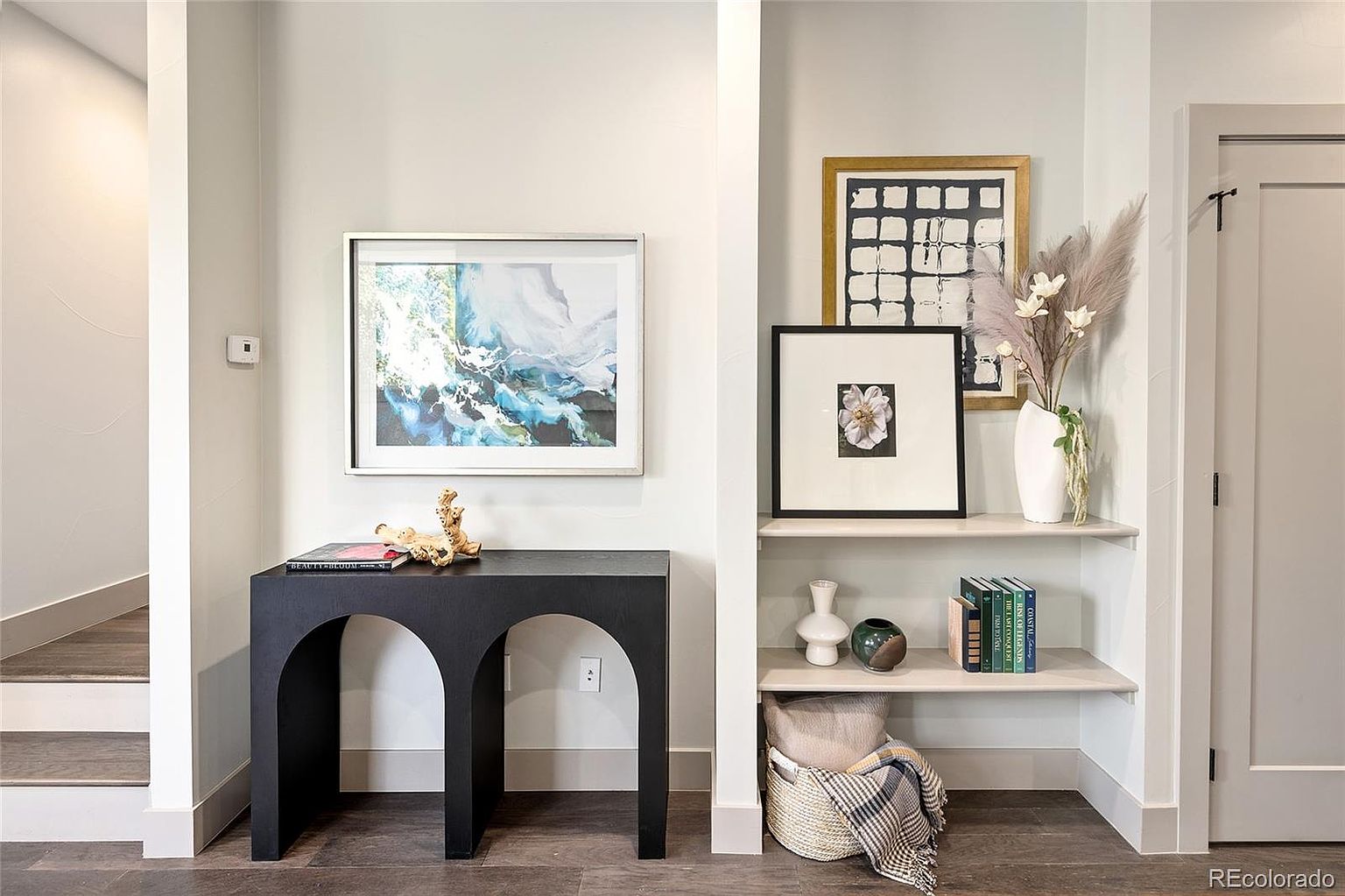 This interior shot showcases a stylish hallway featuring a black console table with artwork above, complemented by built-in shelves displaying decorative items and books. The neutral color palette and modern design create an inviting and sophisticated atmosphere, enhancing the home's appeal. The perspective is from a medium distance, capturing the depth of the hallway and the arrangement of the furniture.