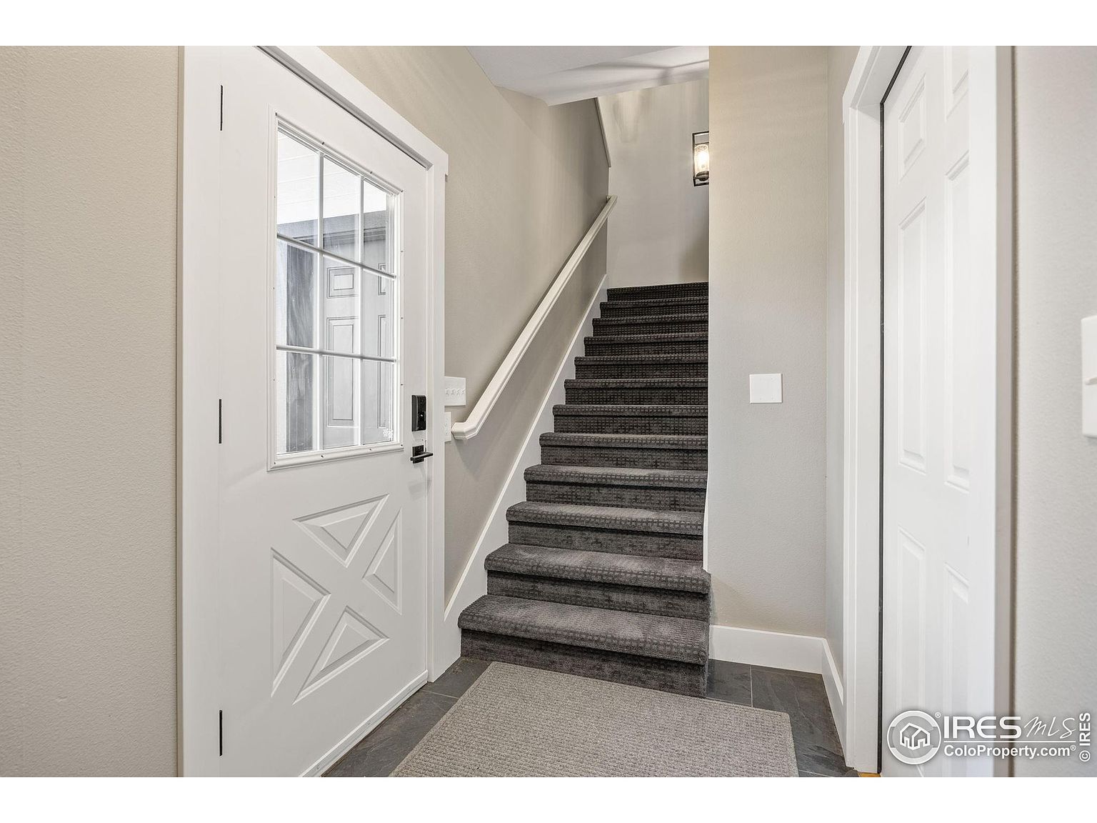 This interior shot showcases a well-lit hallway with carpeted stairs leading upwards. A white door with glass panels is on the left, and another white door is on the right, suggesting access to other rooms. The walls are painted in a neutral tone, creating a clean and inviting atmosphere.