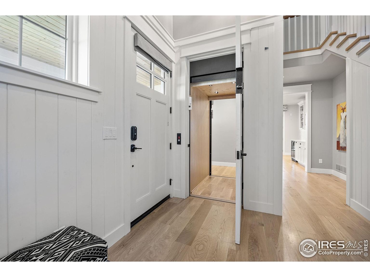 This interior shot showcases a bright and modern entryway featuring light wood flooring and white paneled walls. An elevator is visible, adding a unique and accessible feature to the home. The hallway leads to a staircase and other rooms, creating an open and inviting atmosphere.