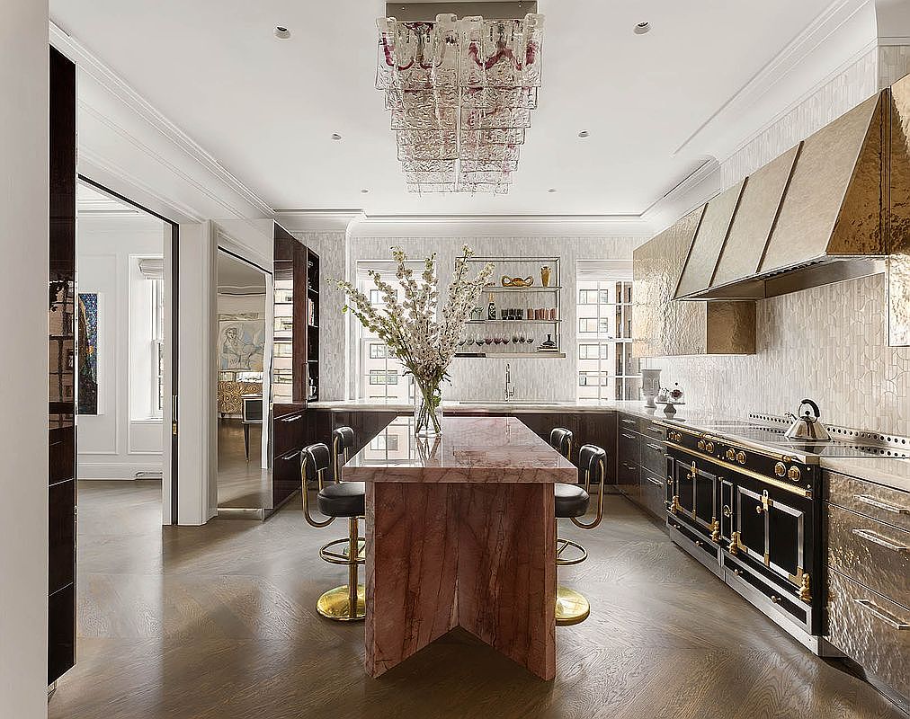 This is a meticulously designed kitchen with high-end finishes. It features a large marble island with seating, a professional-grade range with a custom hood, and custom cabinetry. The room is brightened by natural light and a statement chandelier, creating an elegant and functional cooking space.