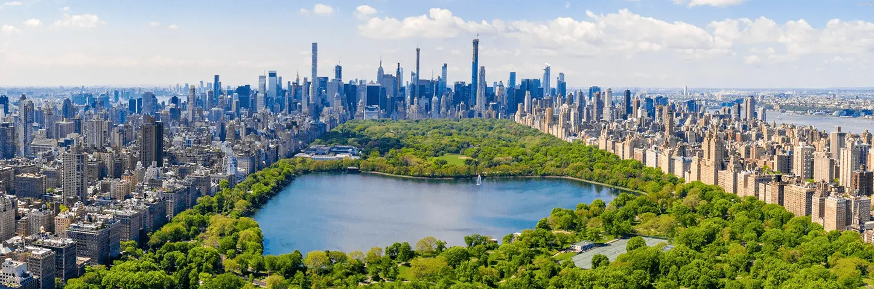 This aerial view showcases a large city skyline with a prominent park and lake. The image captures the scale and proximity of urban development to green spaces, a desirable contrast in city living. It would appeal to buyers seeking a mix of urban convenience and natural environments.